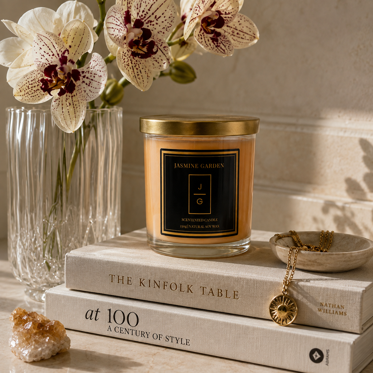 Lumânare parfumată Jasmine Garden din ceară naturală de soia, așezată pe cărți, într-un decor elegant cu orhidee și accesorii aurii.